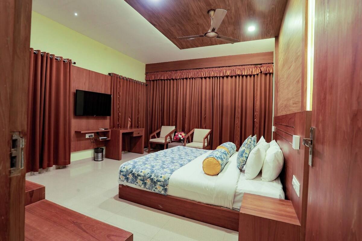 A hotel room with a large bed, a desk, a chair, a TV, and wooden walls.