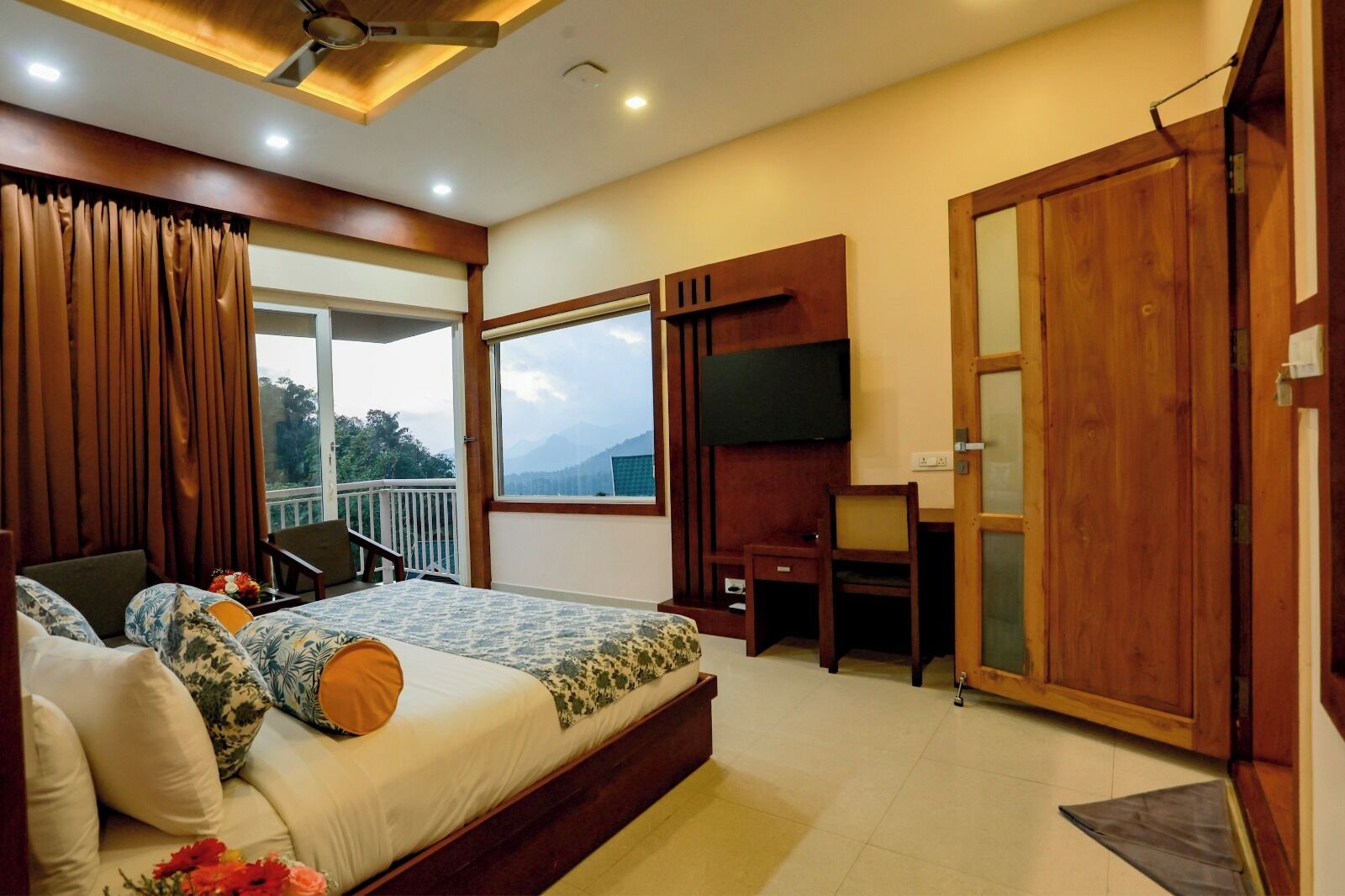 A bedroom with a bed, a desk, a TV, and a balcony with a view.