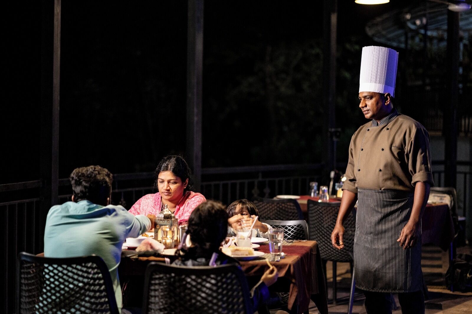 A chef standing by a table with diners.