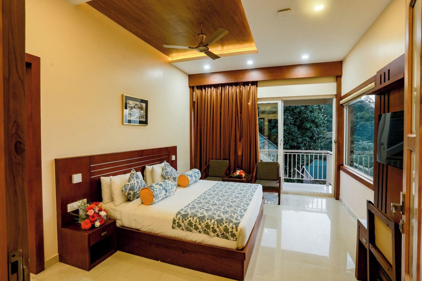 A bedroom with a wooden bed, a nightstand with flowers, a ceiling fan, and a balcony with curtains.