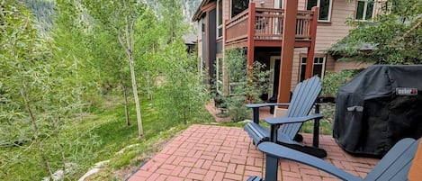 A patio with two Adirondack chairs, a grill, and a view of a mountain.
