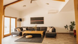 A spacious living room with a high ceiling, wooden beams, a large sofa set, a coffee table, and a potted plant. - A tranquil 40 acre olive grove, comfort inside, fire pit & hot tub outside  (Clare)
