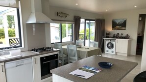 A modern kitchen with a central island, a dining area with a table and chairs, and a laundry area with a washing machine. - Luxuriate in Lumsden (Lumsden)