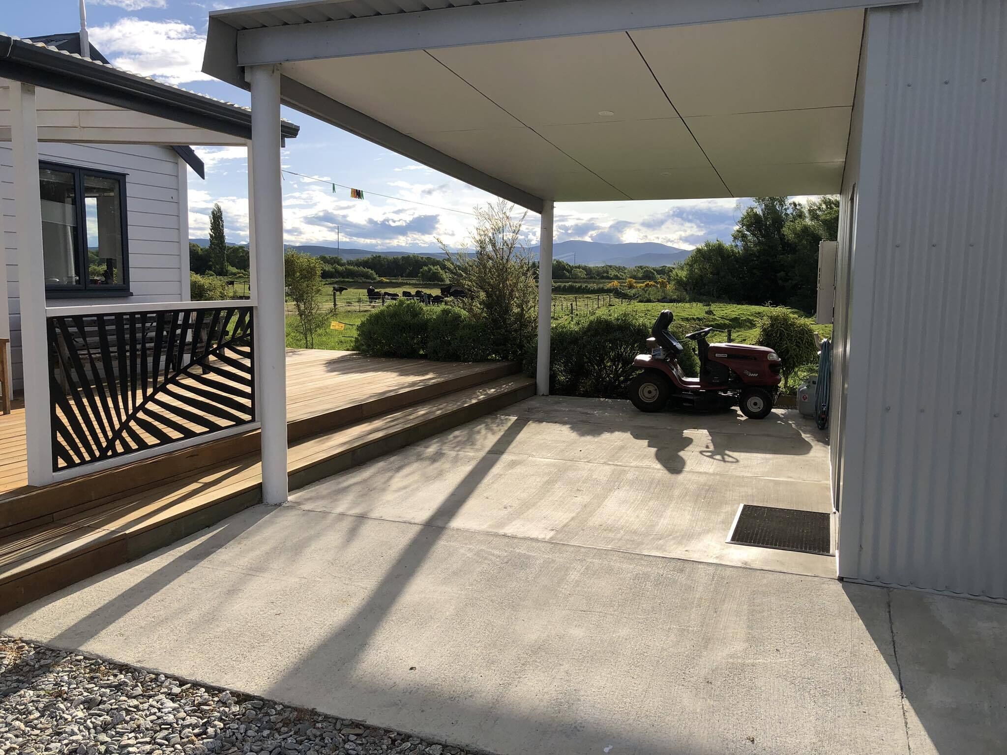 A covered outdoor area with a concrete floor, a wooden deck, and a view of a rural landscape with cows in the distance.
