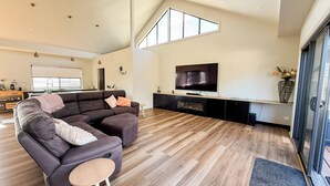 A modern living room with a sectional sofa, a flat-screen TV, and a large window. - Marbles Riverview House (Pet Friendly) Sleeps 10 (Hindmarsh Island)