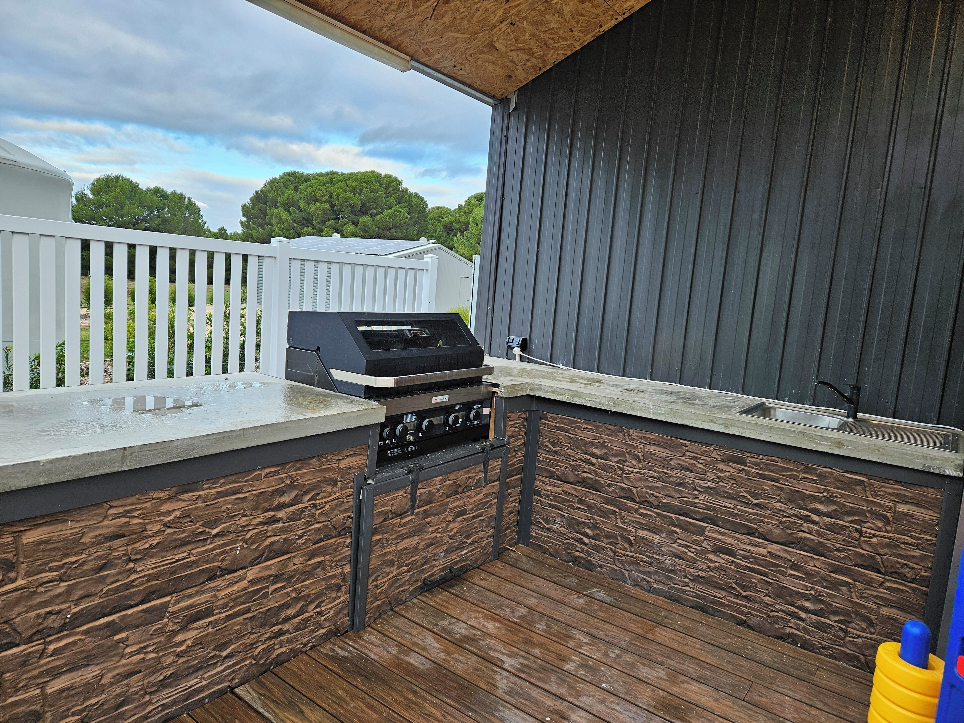 Cucina esterna con barbecue, lavello e terrazza in legno.