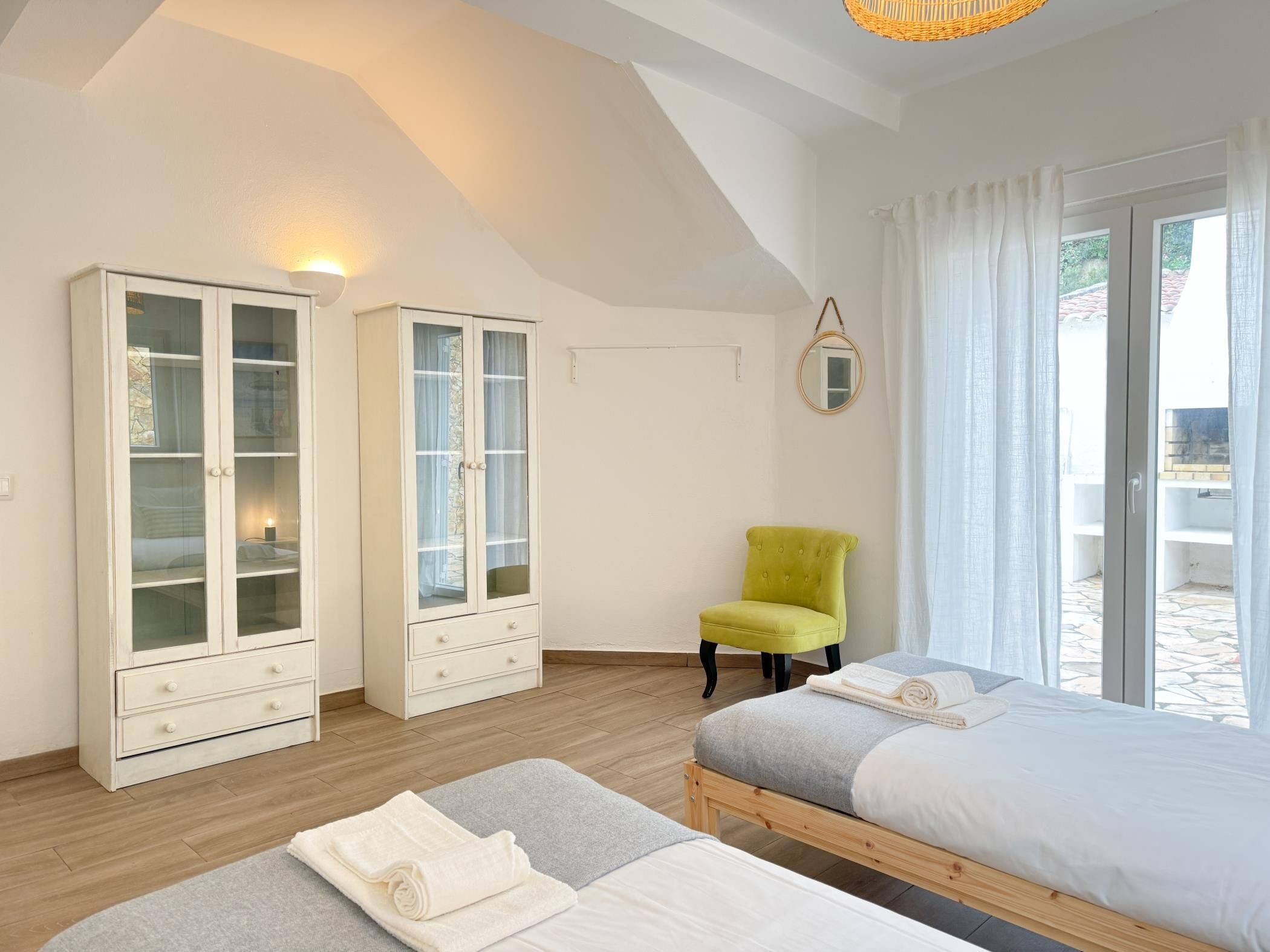 A bedroom with two beds, a wardrobe, a chair, and a large window.