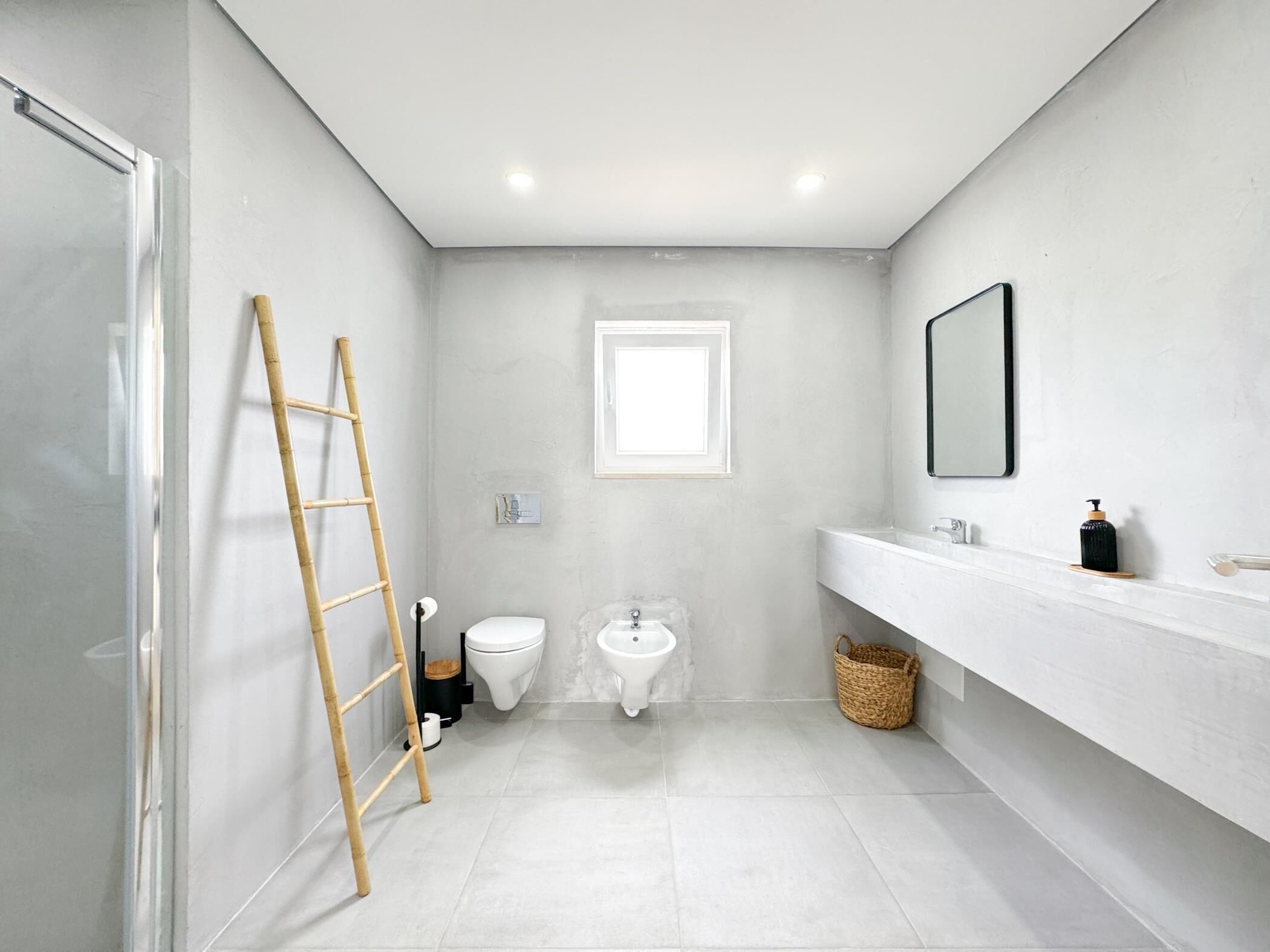 Een moderne badkamer met een wit wastafelmeubel, een spiegel, een toilet en een bidet.