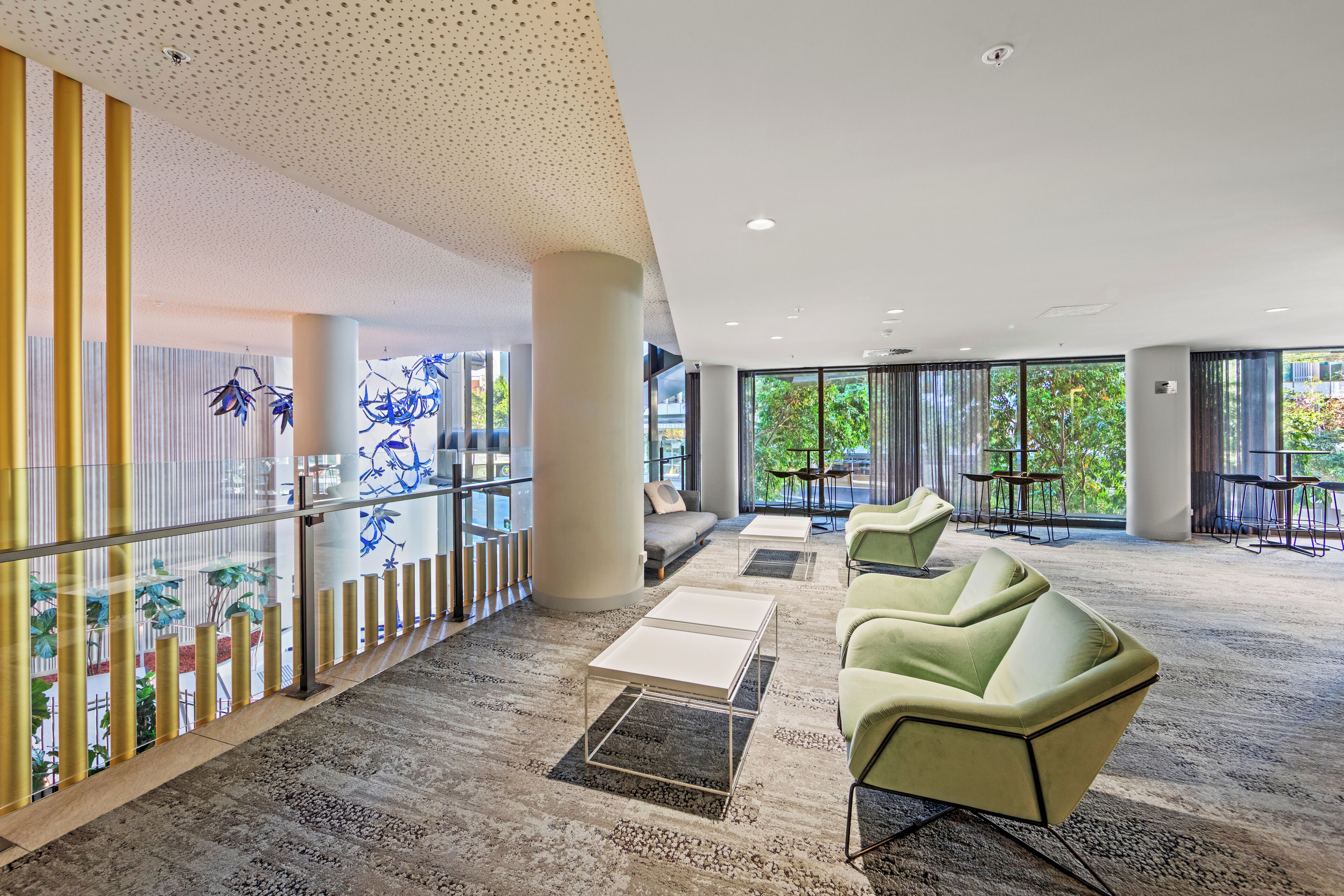 Een ruime lobby met een hoge plafond, een zithoek met stoelen en tafels, en grote ramen met uitzicht op groen buiten.
