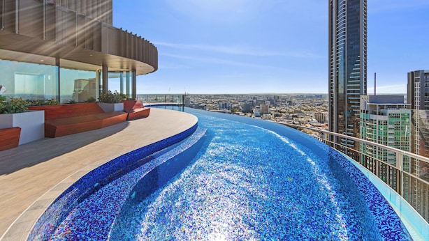 Una piscina infinita en la azotea con vista a la ciudad, arquitectura moderna y cielo despejado.