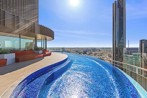 A rooftop infinity pool with a city view, modern architecture, and a clear sky. - Spire Residences by CLLIX (Brisbane)