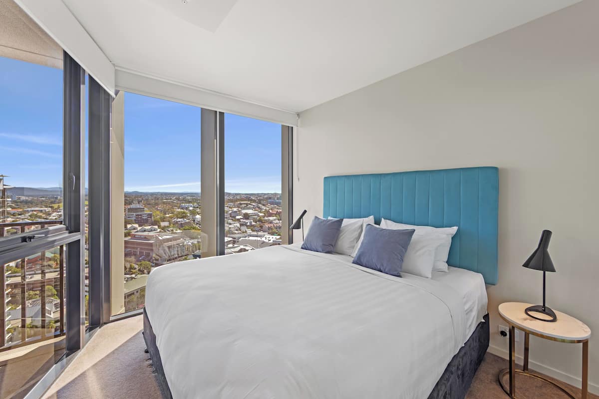 A modern hotel room with a large bed, a view of the city, and a small bedside table.