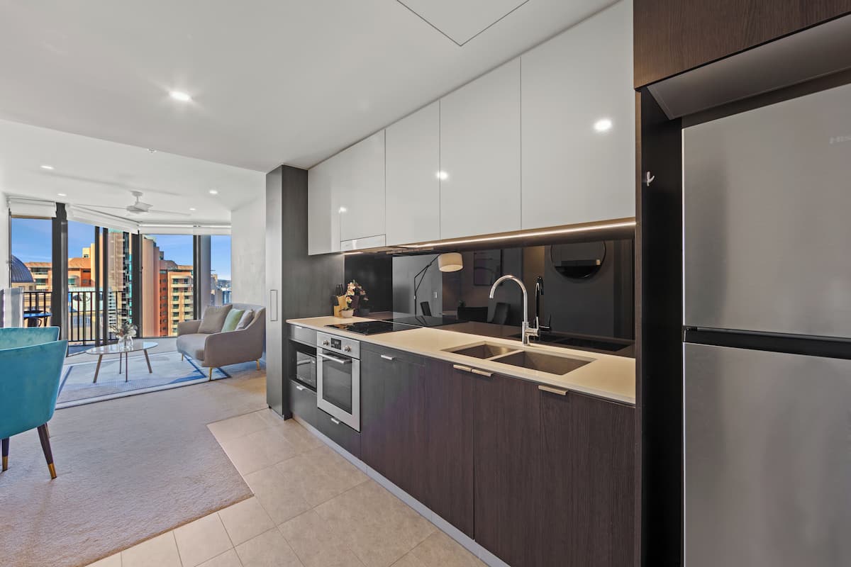 A modern kitchen with dark cabinetry, stainless steel appliances, and a large window offering a city view.