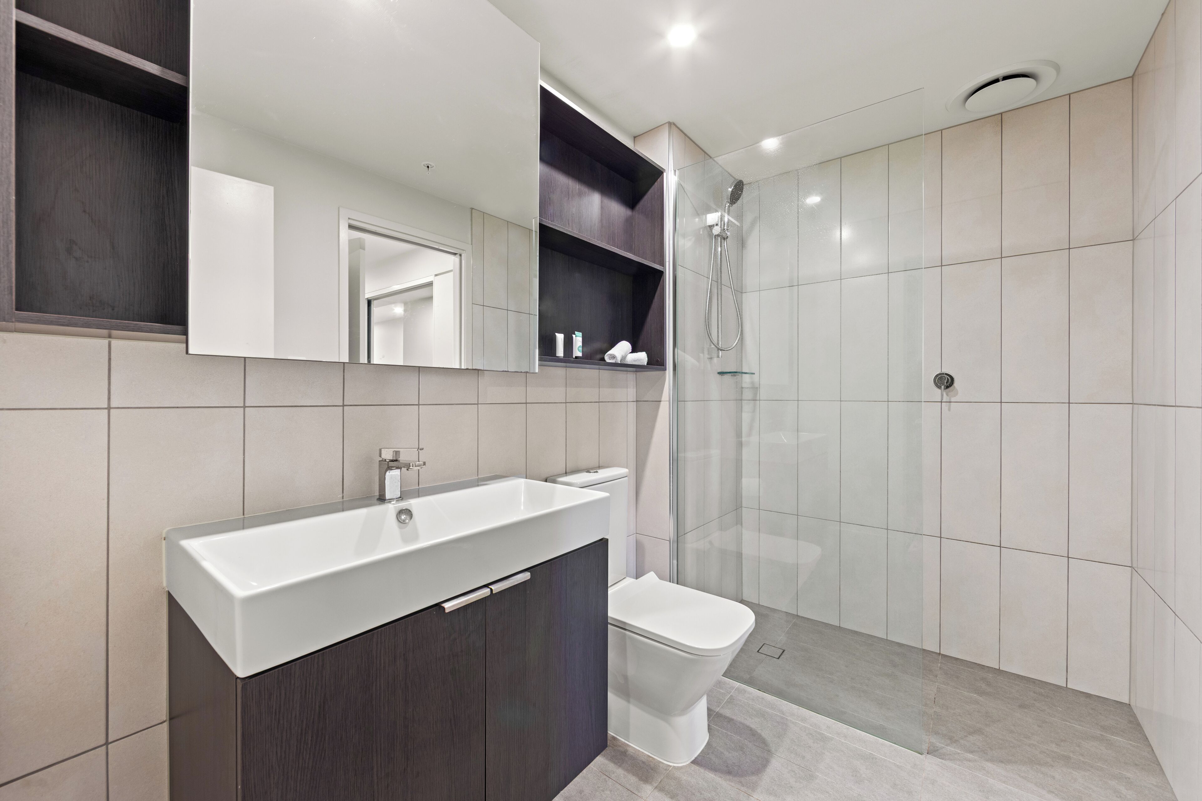 A modern bathroom with a white sink, dark cabinets, a glass shower enclosure, and a toilet.