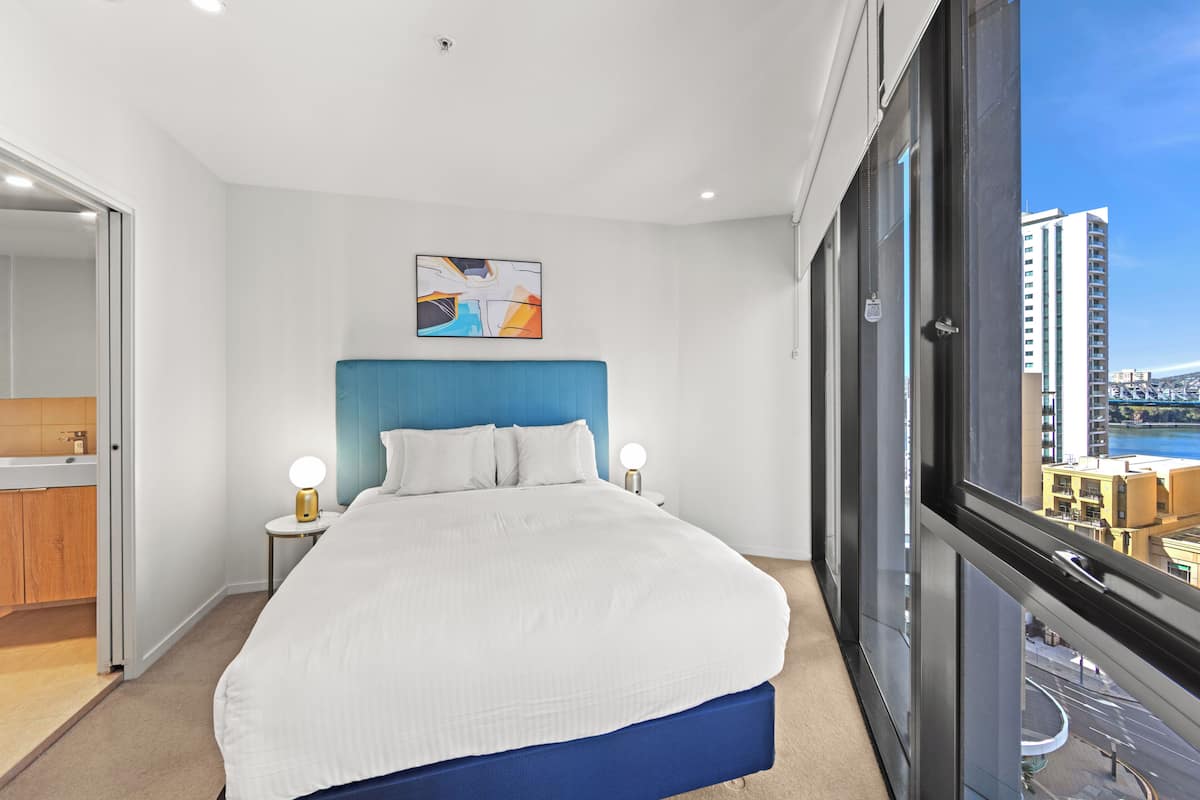 A modern hotel room with a large bed, a view of the city, and a bathroom with a wooden cabinet.