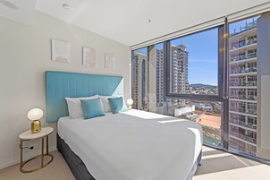 A bedroom with a large bed, a nightstand, a window with a view of buildings, and a ceiling light.