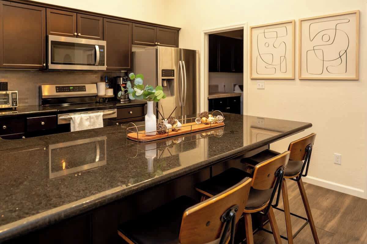 A modern kitchen with dark cabinets, stainless steel appliances, a large island with bar stools, and abstract art on the wall.