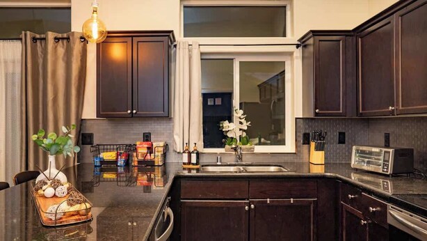 A modern kitchen with dark wood cabinets, a stainless steel sink, and a window with a view of the outside. - Agave Zen House w/ Hot Tub & BBQ Grill! (Porterville)