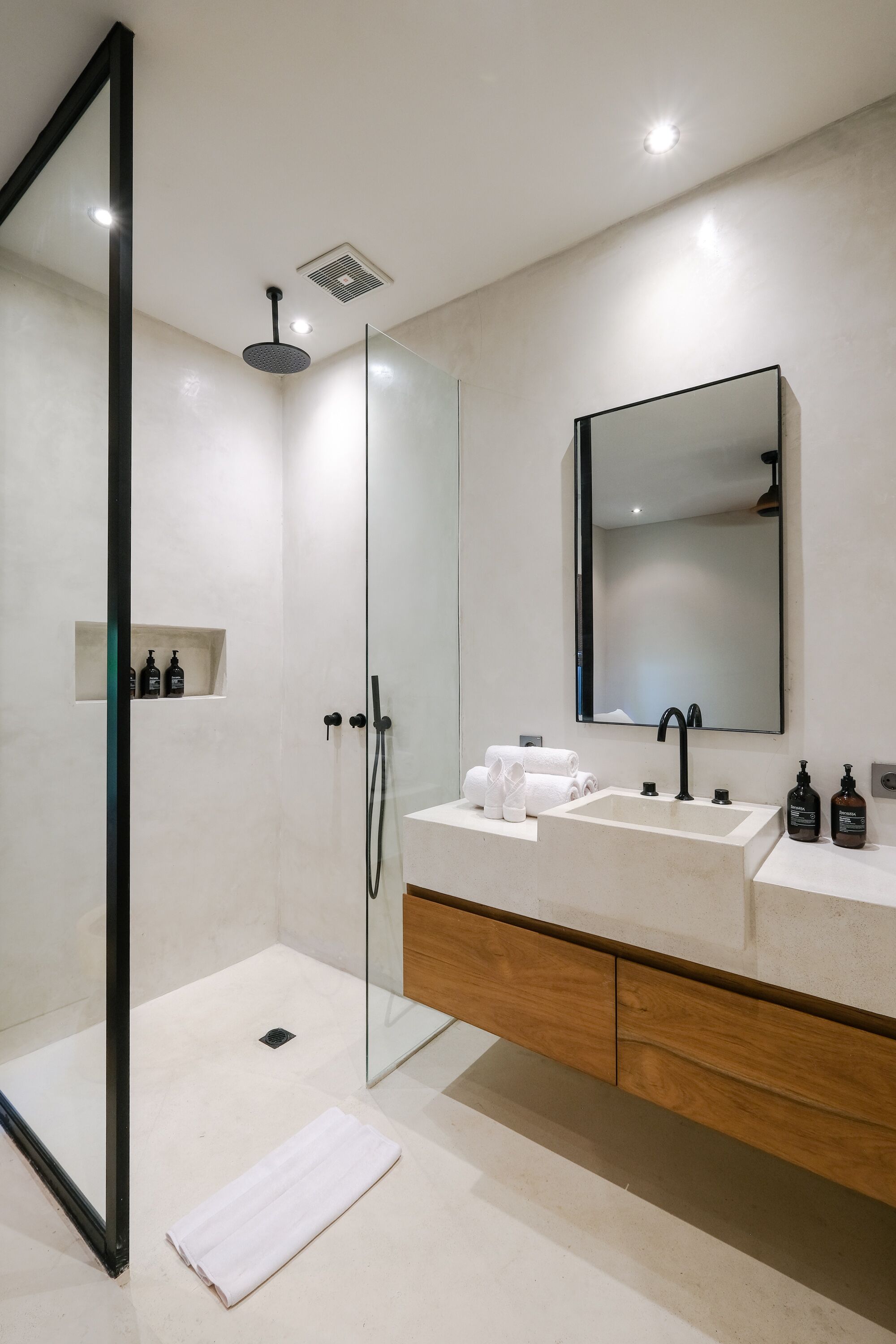 A modern bathroom with a glass-enclosed shower, a large mirror, and a wooden vanity with a sink and two towel racks.