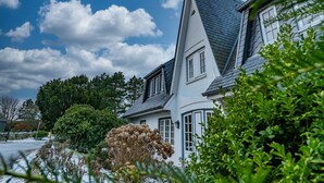 Une maison à deux étages, dotée d’un toit à forte pente, de murs extérieurs blancs et d’un toit foncé.
