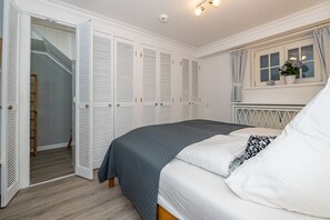 Un dormitorio con cama, contraventanas blancas, una ventana con cortinas y una escalera.