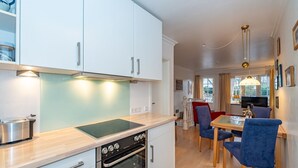 Une cuisine moderne avec des meubles blancs, un four encastré et un coin repas avec des chaises bleues.