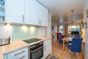 Une cuisine moderne avec des meubles blancs, un four encastré et un coin repas avec des chaises bleues.