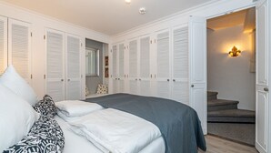 Une chambre à coucher avec un lit, des murs blancs et un placard aux portes à persiennes.