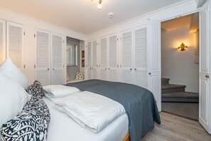 Une chambre à coucher avec un lit, des murs blancs et un placard aux portes à persiennes.