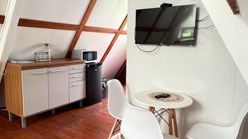 A cozy room with a loft-style ceiling, a TV mounted on the wall, a small dining table with chairs, and a kitchenette area.