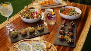 A wooden table with various dishes, including a salad, skewers, and dips, in a restaurant setting. - Boquete Firefly Inn (Los Naranjos)