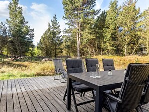 Une terrasse en bois à l’extérieur, avec une table et des chaises, entourée d’une forêt.