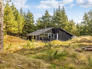 Une cabane moderne dotée d’une grande porte vitrée, entourée de grands arbres et d’un paysage verdoyant.