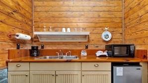 Eine kleine Küche mit Holzwänden, einem Edelstahlspülbecken, einer Kaffeemaschine, einer Mikrowelle und einem Geschirrständer.