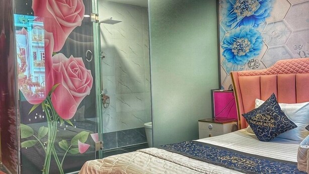 A bedroom with a glass shower, a bed with a pink headboard, and a floral mural on the wall. - Nam Anh Hotel Phu Nhuan -by Bay Luxury (Ho Chi Minh City)