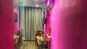 A room with a pink wall, a wooden floor, a ceiling fan, a mirror, and a table with chairs. - Nam Anh Hotel Phu Nhuan -by Bay Luxury (Ho Chi Minh City)