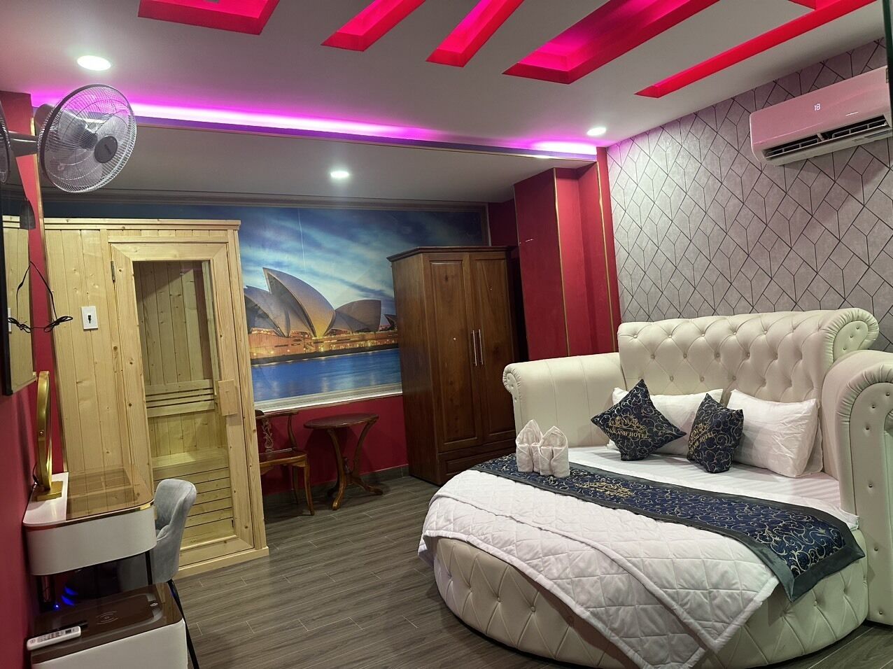 Un dormitorio con cama, escritorio, armario y ventilador.
