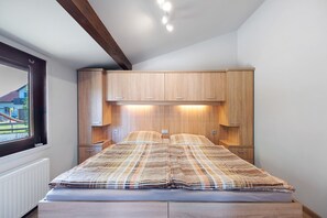 A bedroom with a bed, wooden cabinets, and a window with a view.