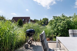 A patio with a grill, a chair, and a house in the background.