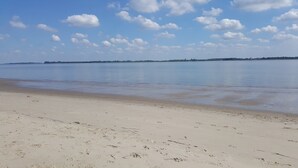 Ein weiter Sandstrand mit ruhigem Wasser und blauem Himmel.