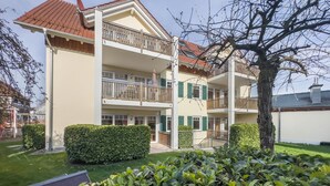 Um edifício residencial com vários andares, varandas, um gramado bem cuidado e uma árvore em primeiro plano.