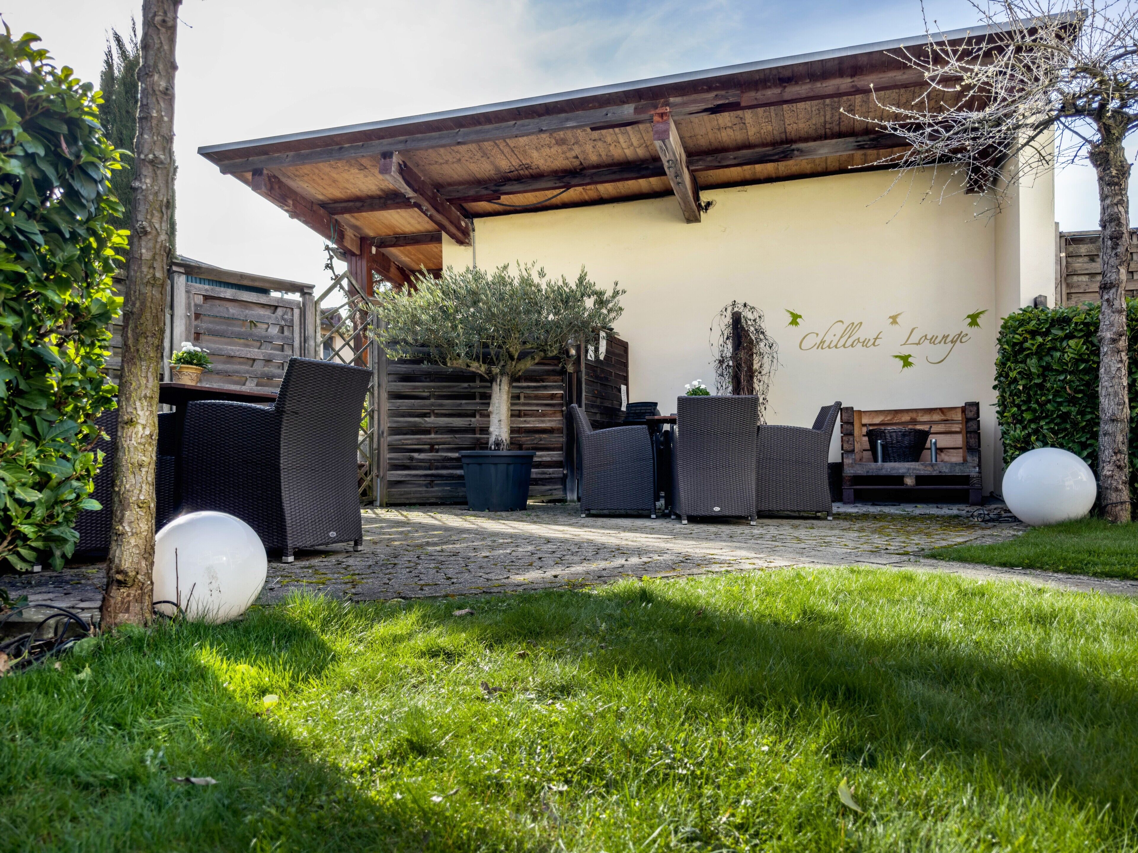 Een terras met rieten meubels, een houten bankje en een muur met de tekst 'Chillout Lounge'.