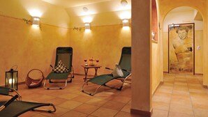 Een wellnessruimte met twee ligstoelen, een klein tafeltje met drankjes en een massage tafel aan de muur bevestigd.