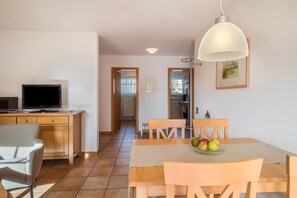 Un coin repas comprenant une table, des chaises, un téléviseur et un panier de fruits.