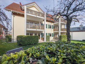 Un immeuble résidentiel à plusieurs étages, doté de balcons, d’une pelouse bien entretenue et d’un arbre au premier plan.