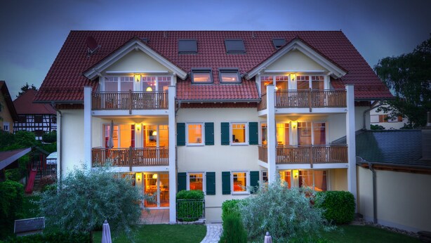 Een gebouw met twee verdiepingen, balkons, een tuin en een pad dat naar de ingang leidt.