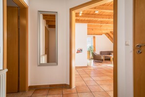 Un pasillo con puerta de madera, un espejo y vista a un salón con sofá y planta.