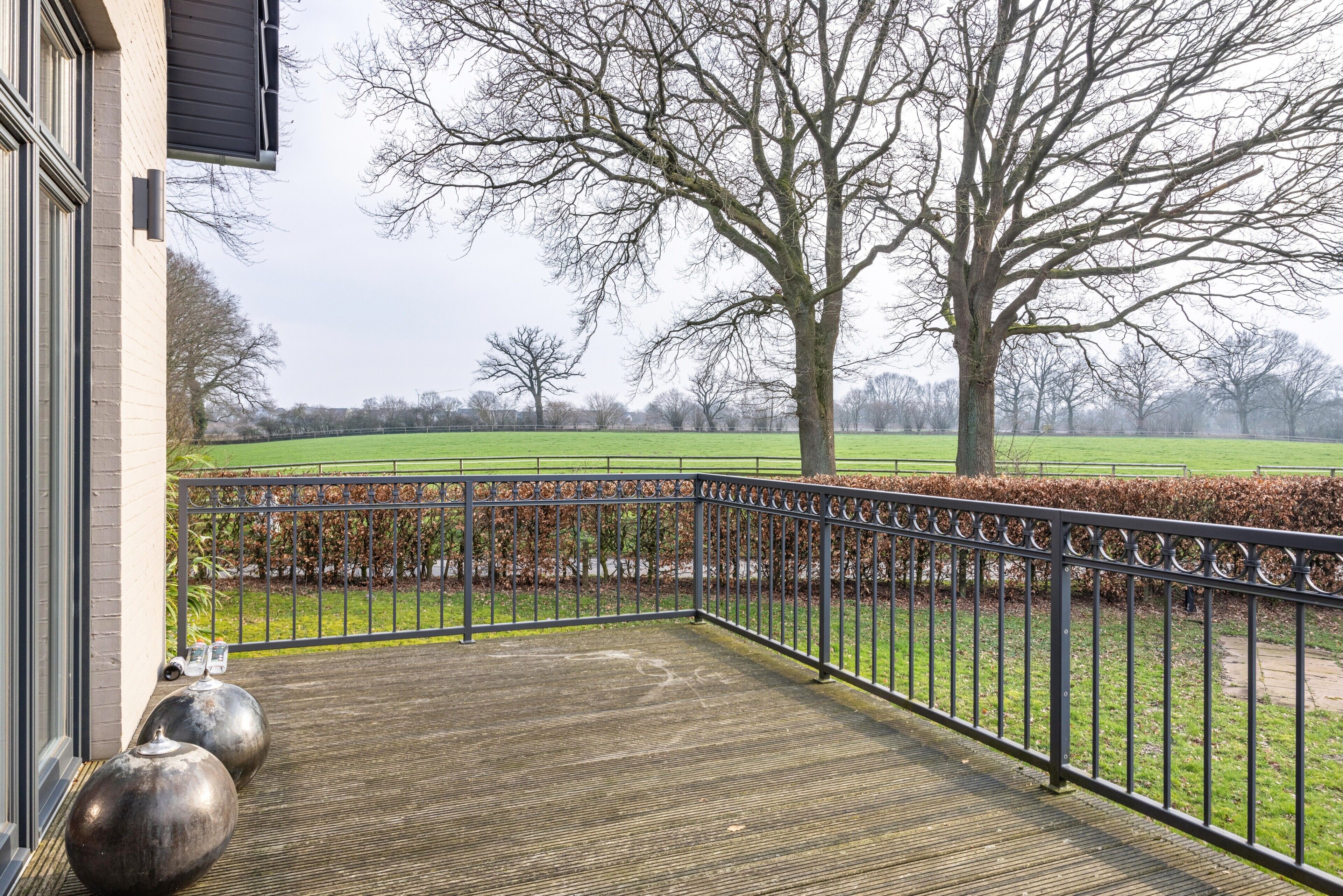 A balcony with a view of a green field and trees.