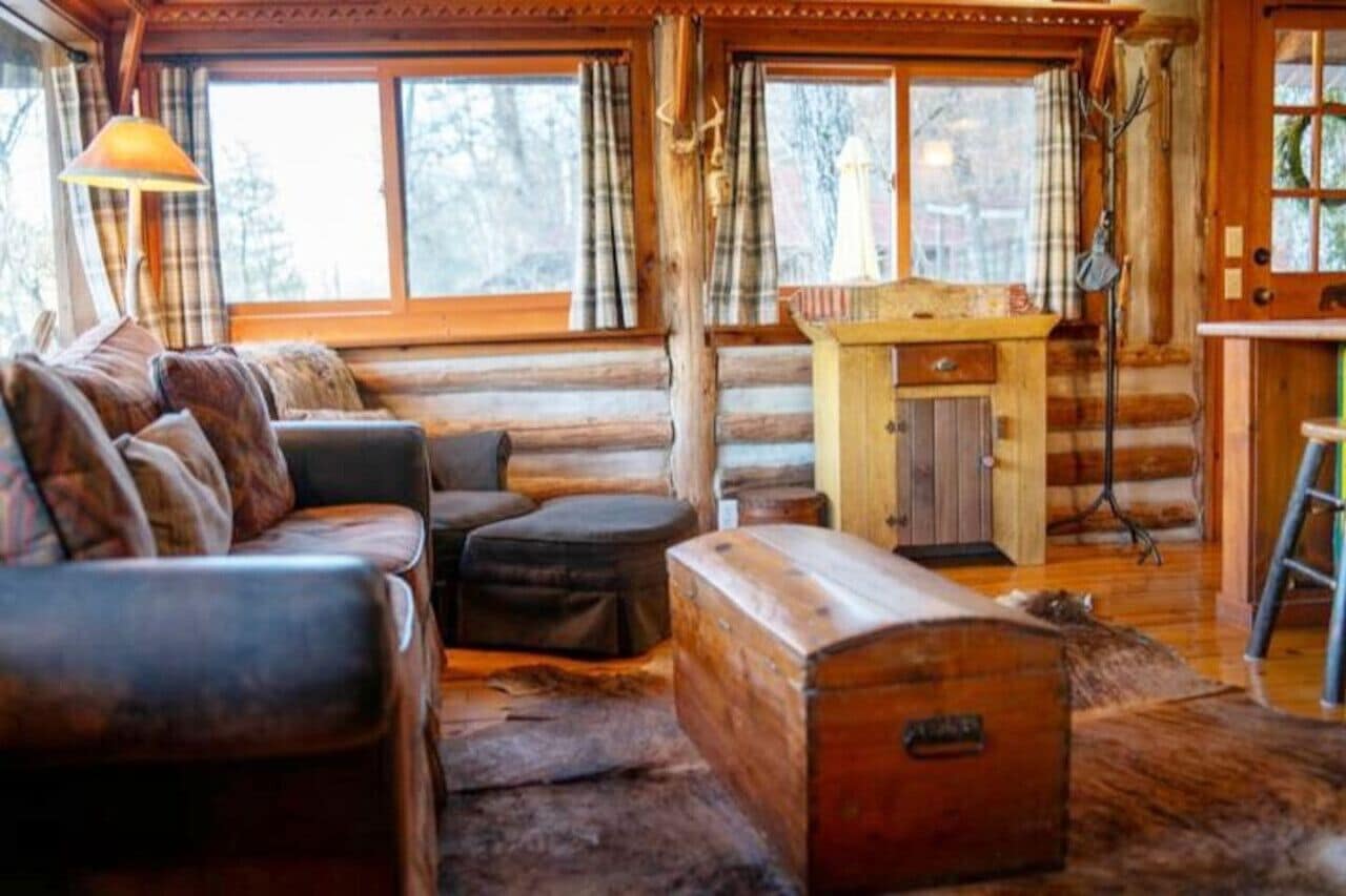 L’intérieur d’une cabane en rondins, avec un canapé en cuir, une table en bois et un rideau à carreaux.