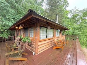 A log cabin with a wooden deck, two rocking chairs, and a chimney.
